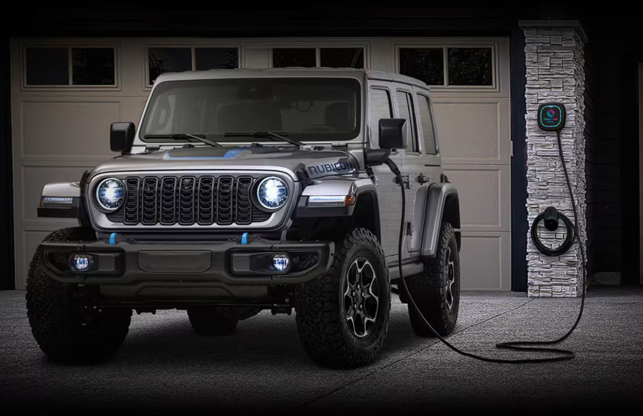 One of the new black electric Jeeps connected to its charger with the front headlights on