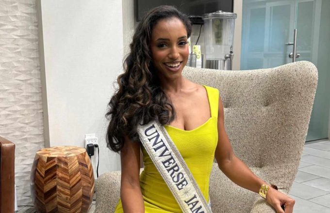 A young Miss Jamaica posing for the camera while sitting on a white armchair and wearing a beautiful fitted yellow dress