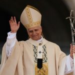 The pope greeting his audience while leaning out from one of the balconies of the Vatican