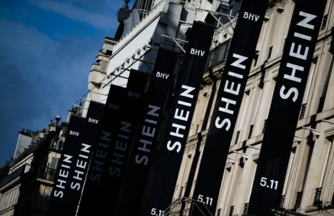 A building with several black banners hanging down, each displaying the word “SHEIN” in bold white letters