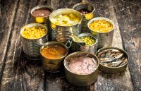 Different canned foods on a table, including tuna, fruit, vegetables, and sardines