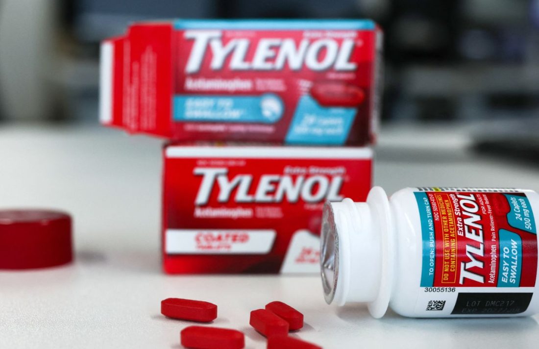 A bottle of Tylenol lying on a table with some pills scattered around and two boxes of the same medication in the background