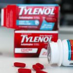 A bottle of Tylenol lying on a table with some pills scattered around and two boxes of the same medication in the background