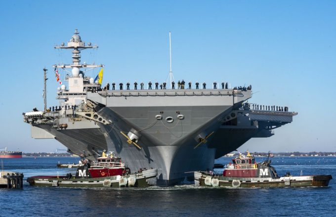A front-view shot of the incredible warship as it is being guided by several smaller tugboats