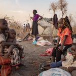 People from the country of Sudan sitting on the sand under the scorching sun