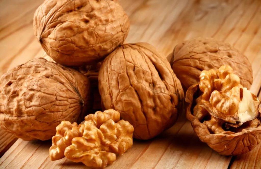 Several walnuts on a table, some with shells and others opened and ready to eat