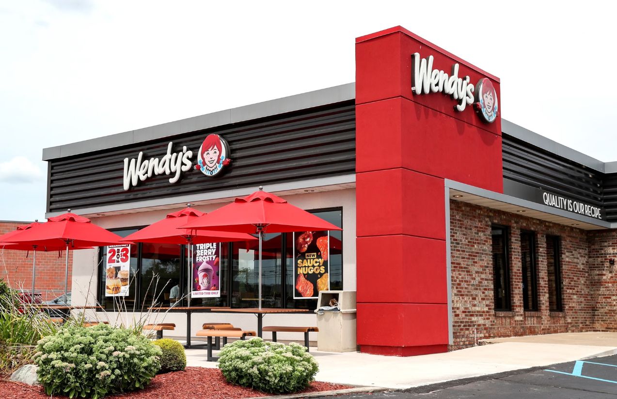 One of Wendy’s franchise locations featuring several outdoor tables with umbrellas and its signature red color tone