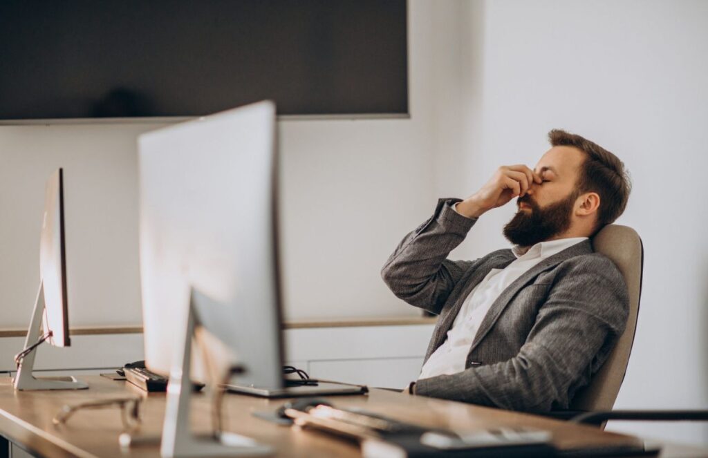 A person in their office in front of their computer showing signs of stress