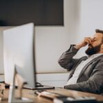 A person in their office in front of their computer showing signs of stress