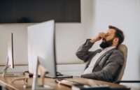 A person in their office in front of their computer showing signs of stress