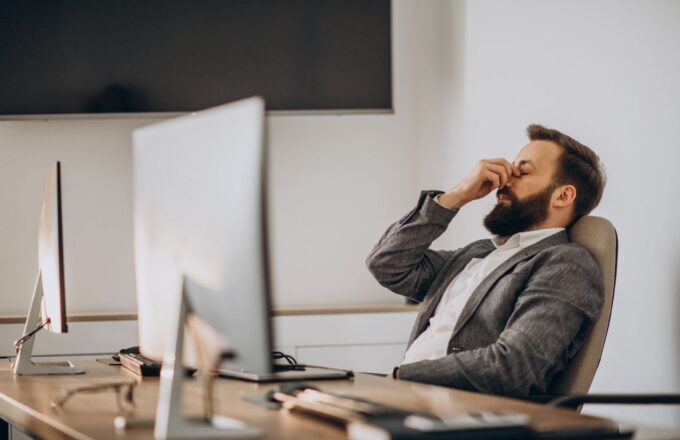 A person in their office in front of their computer showing signs of stress