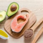 Some healthy foods such as fish, avocado, and various seeds placed on a table