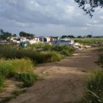 A panoramic view of a meadow in deplorable conditions, with lots of trash and a few people walking around