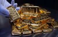 A gloved hand holding several gold bars resting on a table