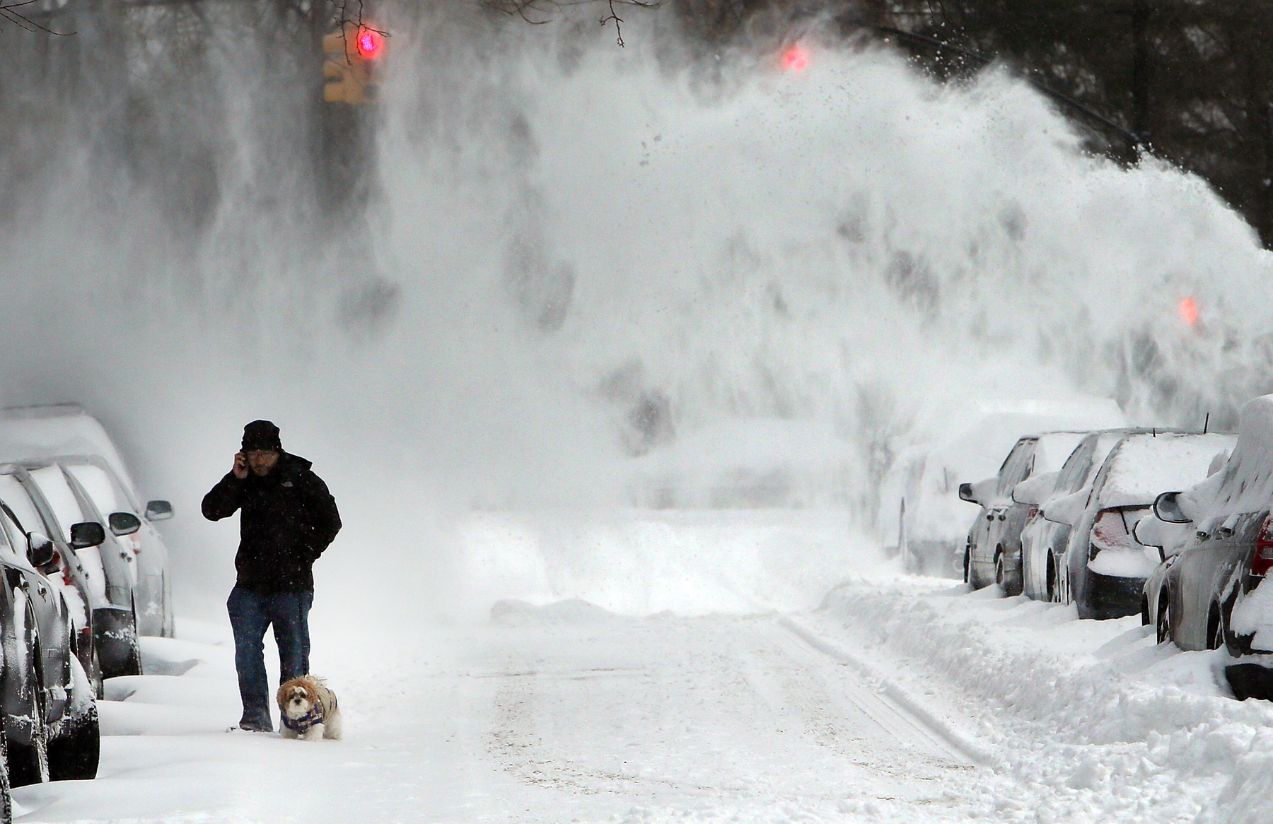 A person walking down a snow-covered street with many parked cars