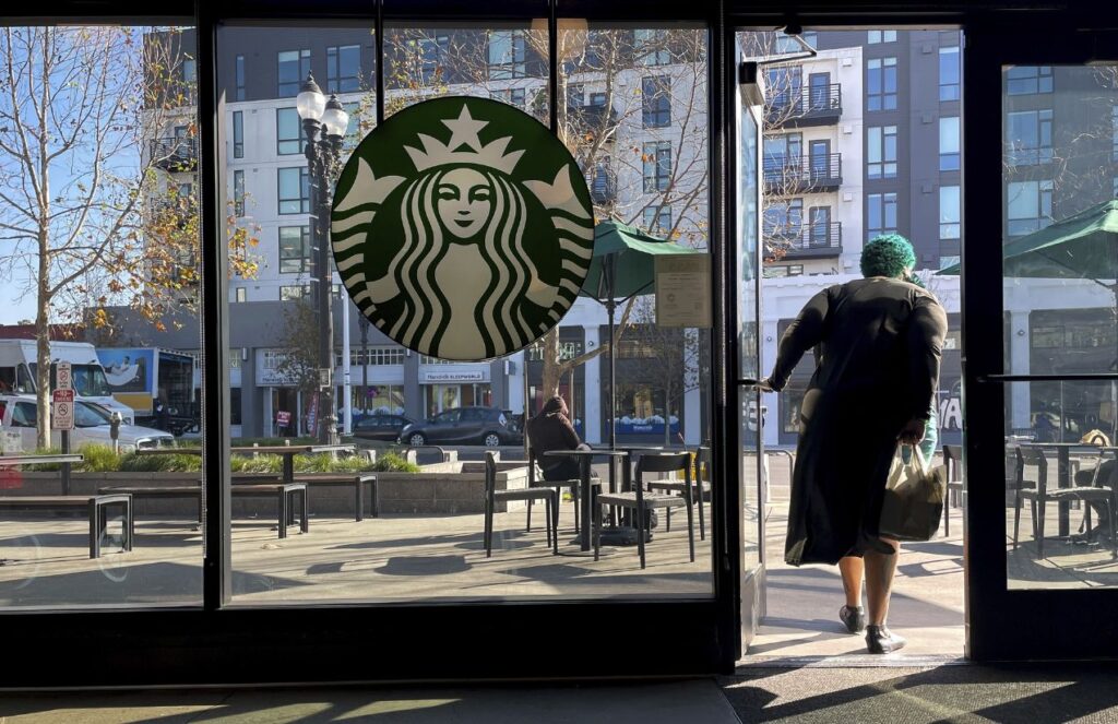 A person walking out of a Starbucks store with very large windows and the logo centered on one of them