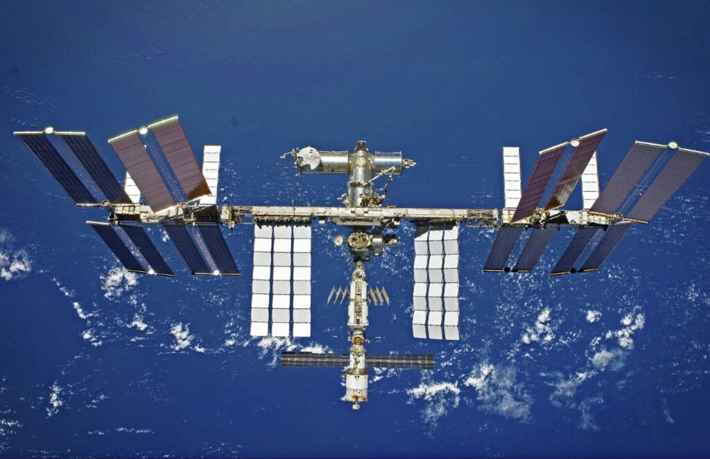 A panoramic image of the International Space Station in the vastness of space, with planet Earth nearby