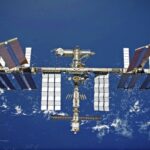 A panoramic image of the International Space Station in the vastness of space, with planet Earth nearby
