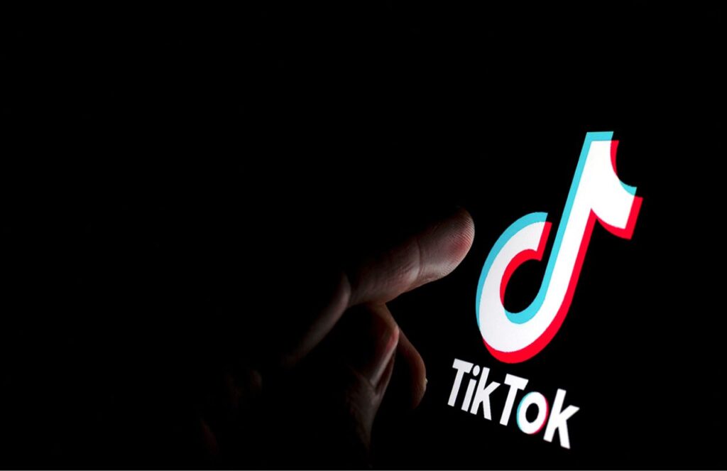TikTok reaches a deal to sell its United States operations after years of conflict A completely dark room with a person holding a phone with the TikTok app open