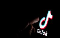 A completely dark room with a person holding a phone with the TikTok app open