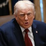 Donald Trump with an angry expression, sitting in an office, wearing an elegant suit