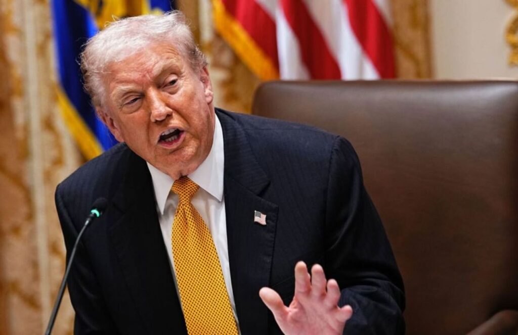 Donald Trump speaking loudly in front of a microphone and a large crowd
