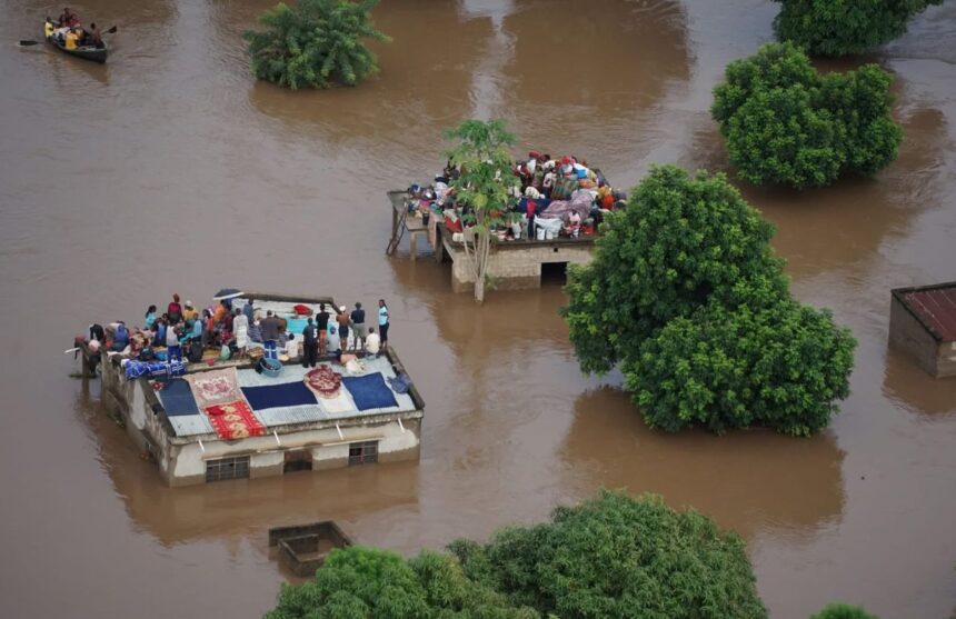 Houses submerged in floodwaters, with people standing on rooftops to avoid being swept away