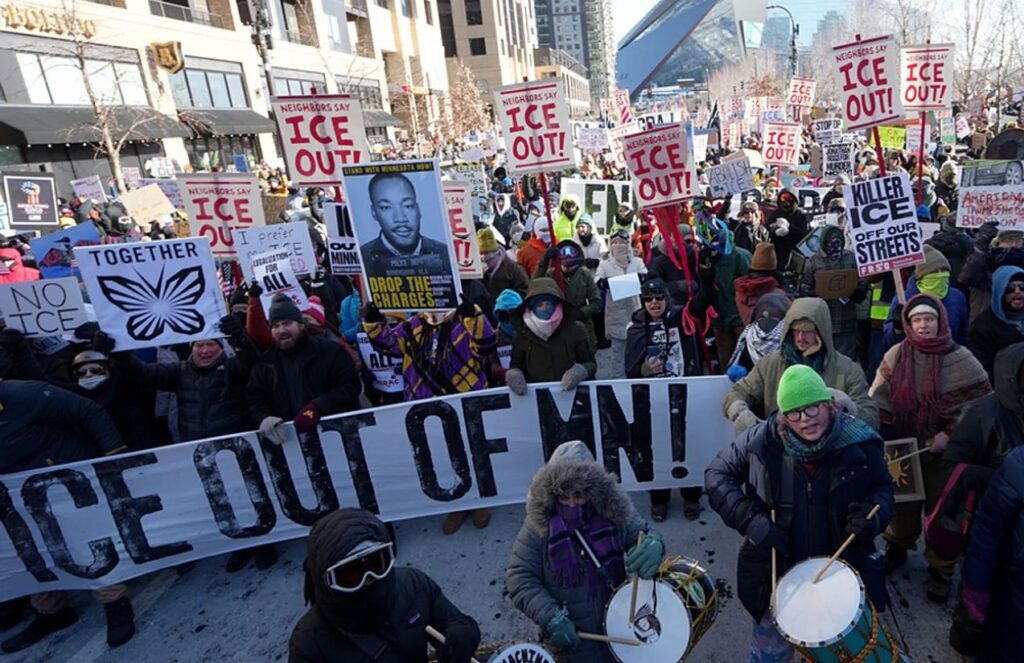 Many people in the United States protesting against ICE, holding signs that read “ICE Out.”