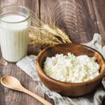 A glass filled with kefir, and next to it a bowl of the same product, slightly thicker, all placed on a table