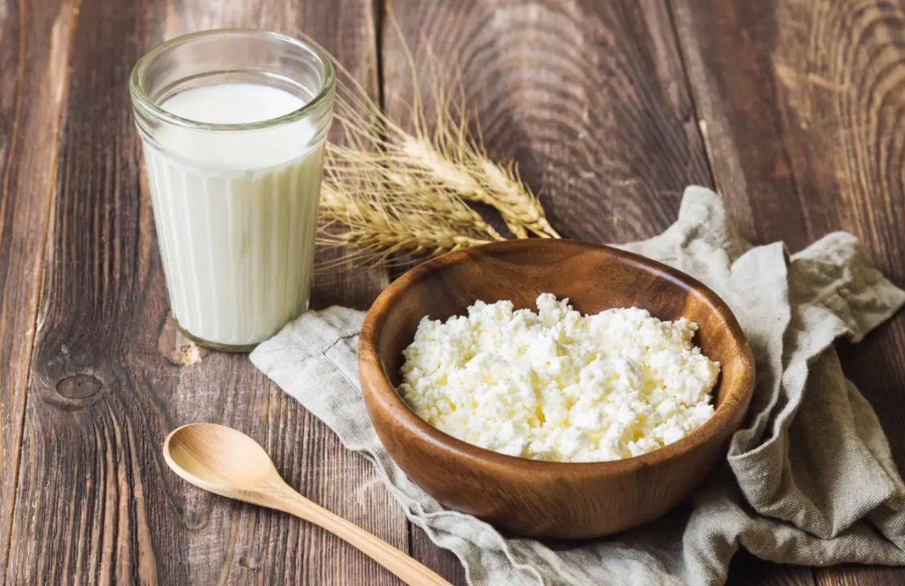 A glass filled with kefir, and next to it a bowl of the same product, slightly thicker, all placed on a table