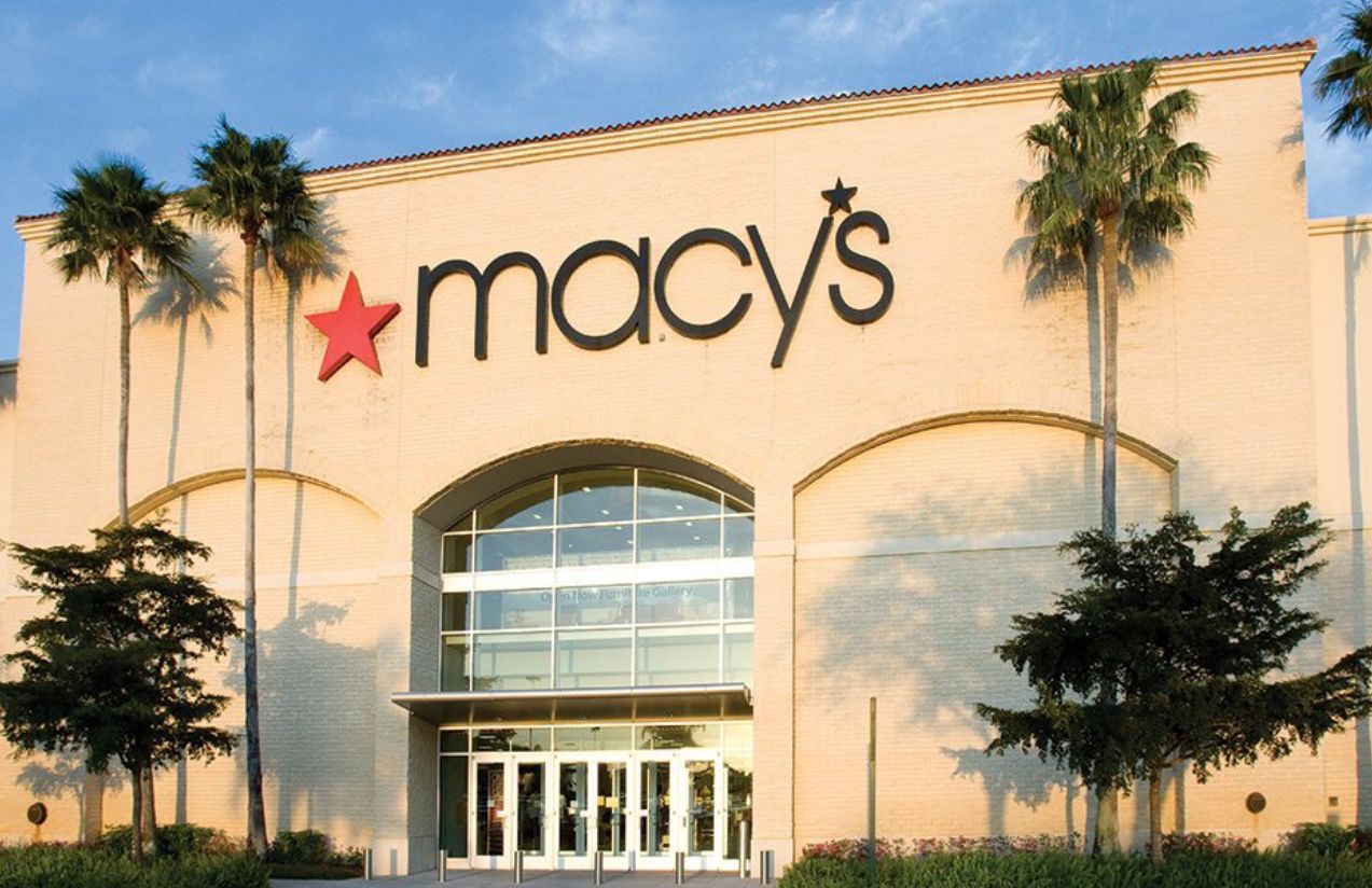 A panoramic view of a large Macy’s store with its red logo and a beige-colored building