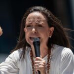 The Venezuelan opposition leader encouraging her supporters while speaking into a microphone with a firm and determined tone