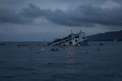 A ferry slowly sinking while its passengers, in the water, watch it go down