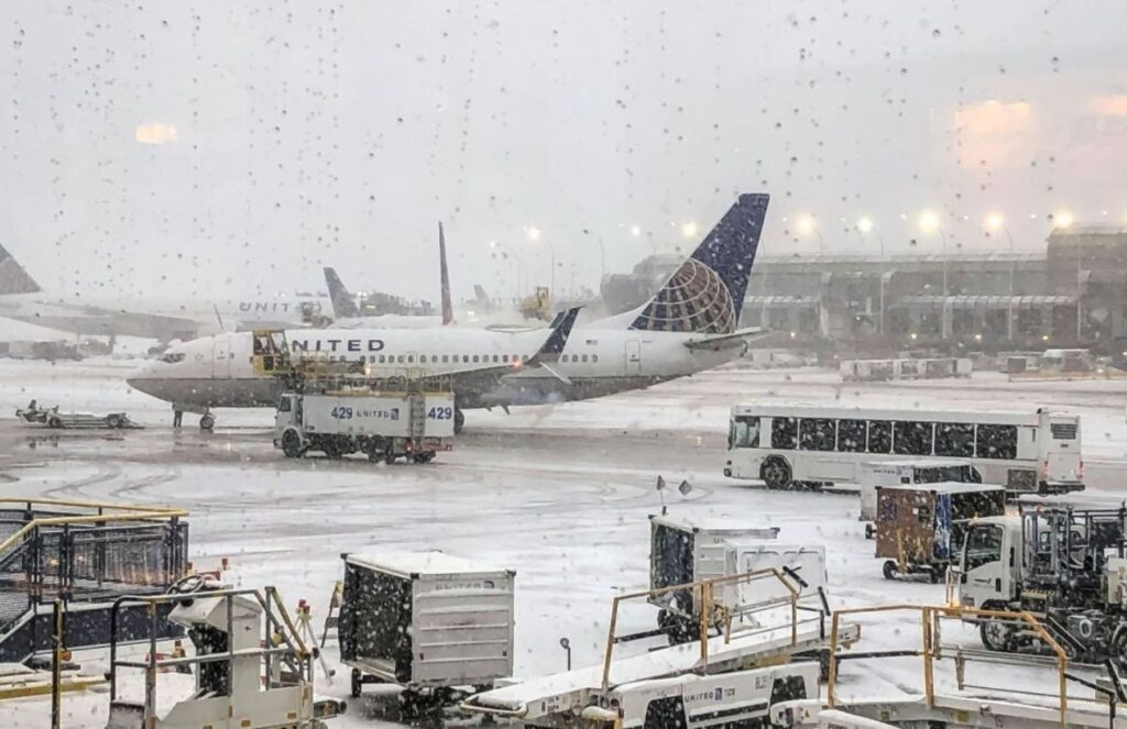 An airplane covered in snow and surrounded by several security vehicles