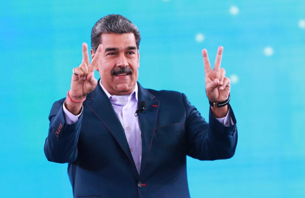 Nicolás Maduro greeting his supporters during a press conference, raising his fingers in a peace sign