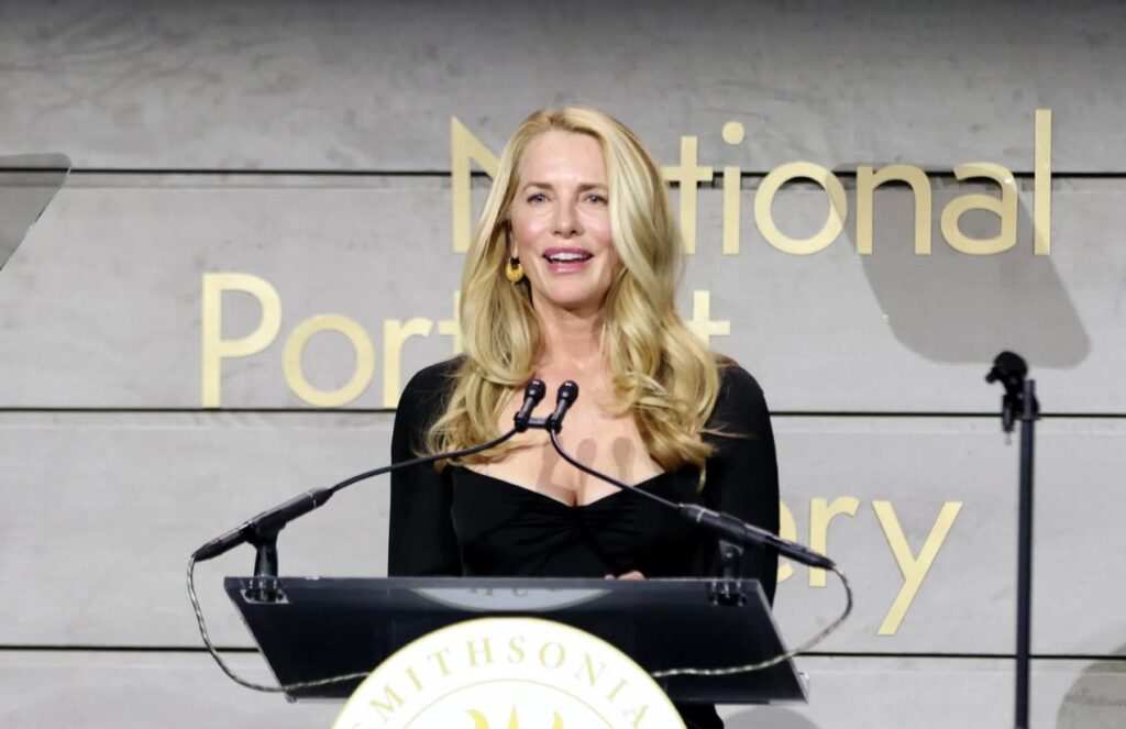 Powell Jobs on a stage, standing on a platform and giving a talk to a large audience, wearing an elegant suit