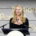 Powell Jobs on a stage, standing on a platform and giving a talk to a large audience, wearing an elegant suit