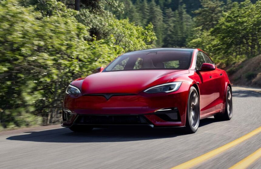 A red Tesla Model S driving alone at high speed on a road