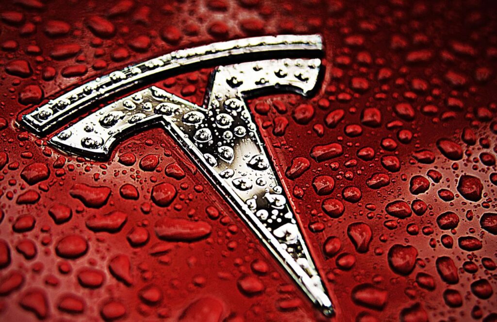 The Tesla logo on a red car with many droplets on the front of the vehicle