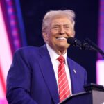 Trump standing behind a podium, smiling at the crowd that is supporting him