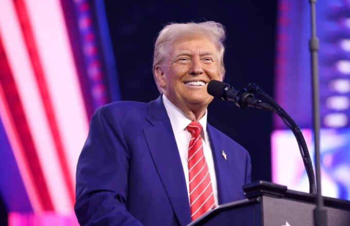 Trump standing behind a podium, smiling at the crowd that is supporting him