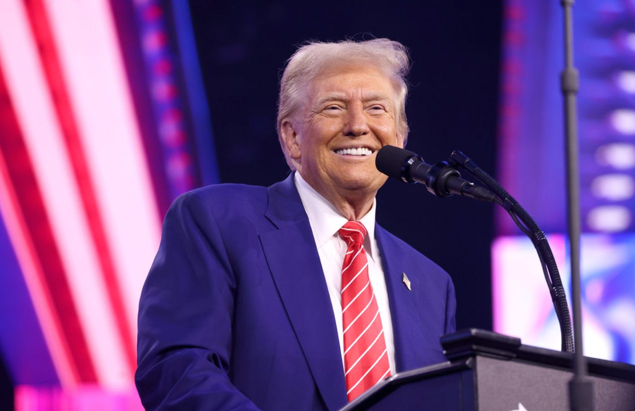 Trump standing behind a podium, smiling at the crowd that is supporting him