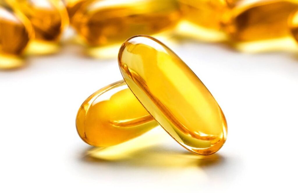Two omega-3 capsules stacked on top of each other, with many more piled up behind them