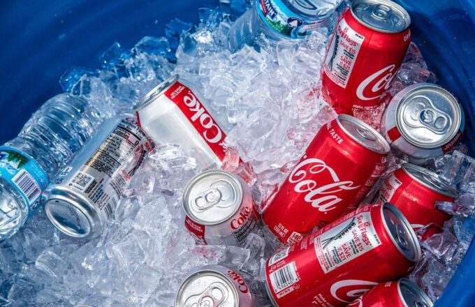 Several Coca-Cola cans inside a cooler filled with lots of ice