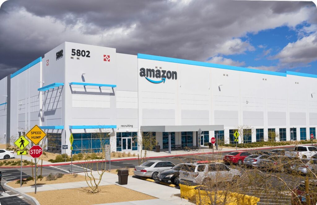 A panoramic view of a white Amazon company building with the word “Amazon” displayed above in black and blue