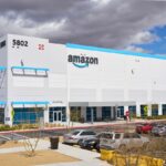 A panoramic view of a white Amazon company building with the word “Amazon” displayed above in black and blue