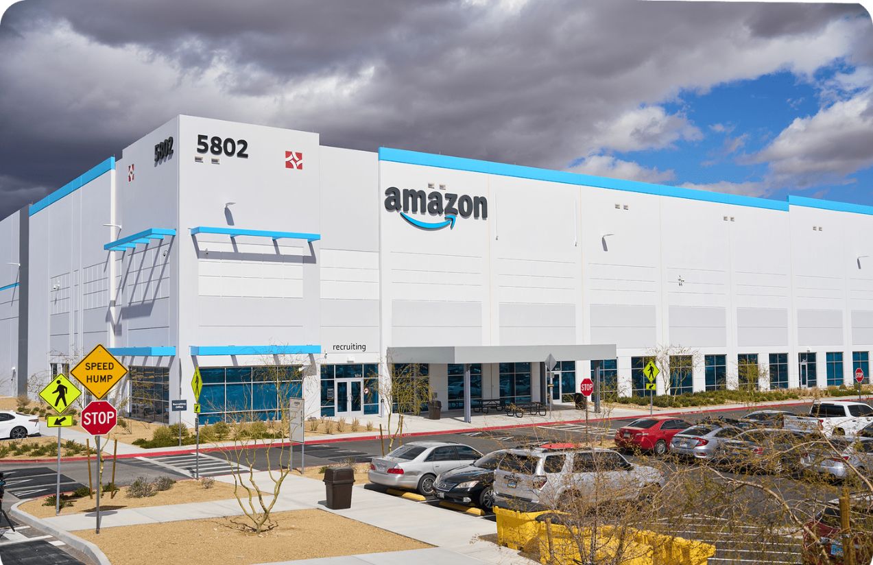 A panoramic view of a white Amazon company building with the word “Amazon” displayed above in black and blue