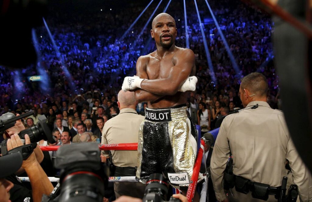 Floyd standing on the ropes of a boxing ring celebrating another victory in his career
