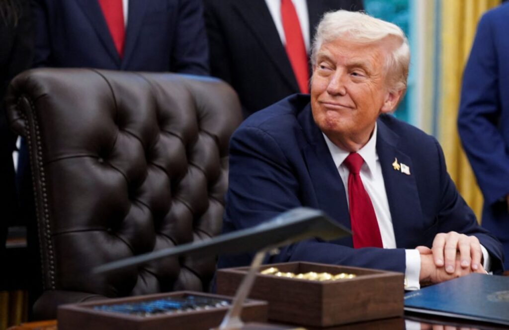 Donald Trump seated in his presidential office surrounded by many people
