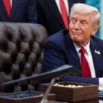 Donald Trump seated in his presidential office surrounded by many people